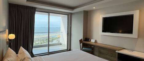 Quarto de hotel com uma cama grande, uma mesa de escritório, uma televisão de tela plana e vista para a cidade pela janela.