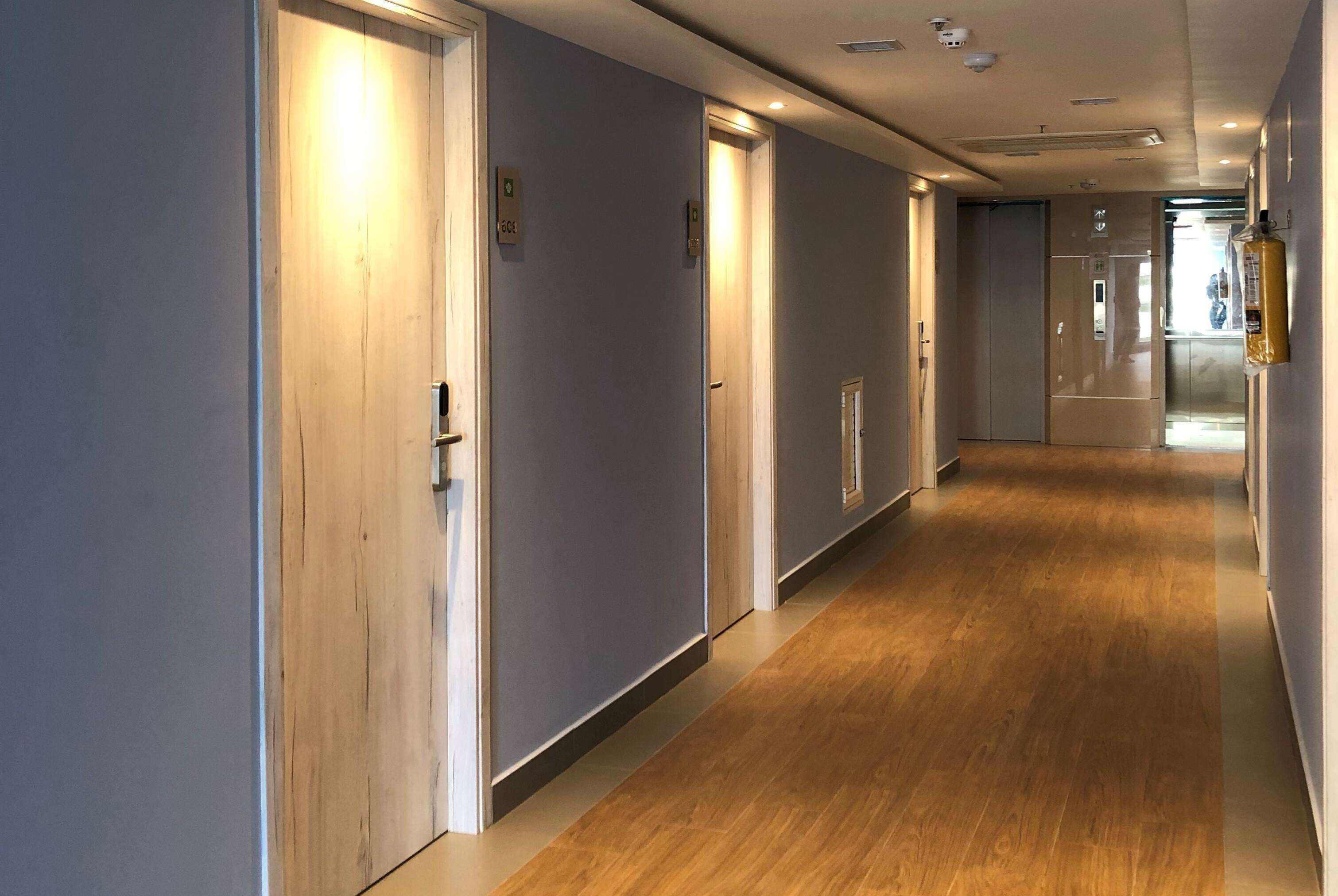 A modern hallway with wooden flooring, light-colored walls, and doors with emergency exit signs.