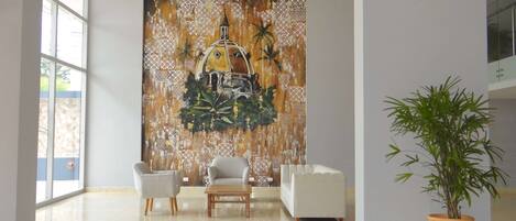 A spacious lobby with a large mural, a seating area with a coffee table, and a potted plant.
