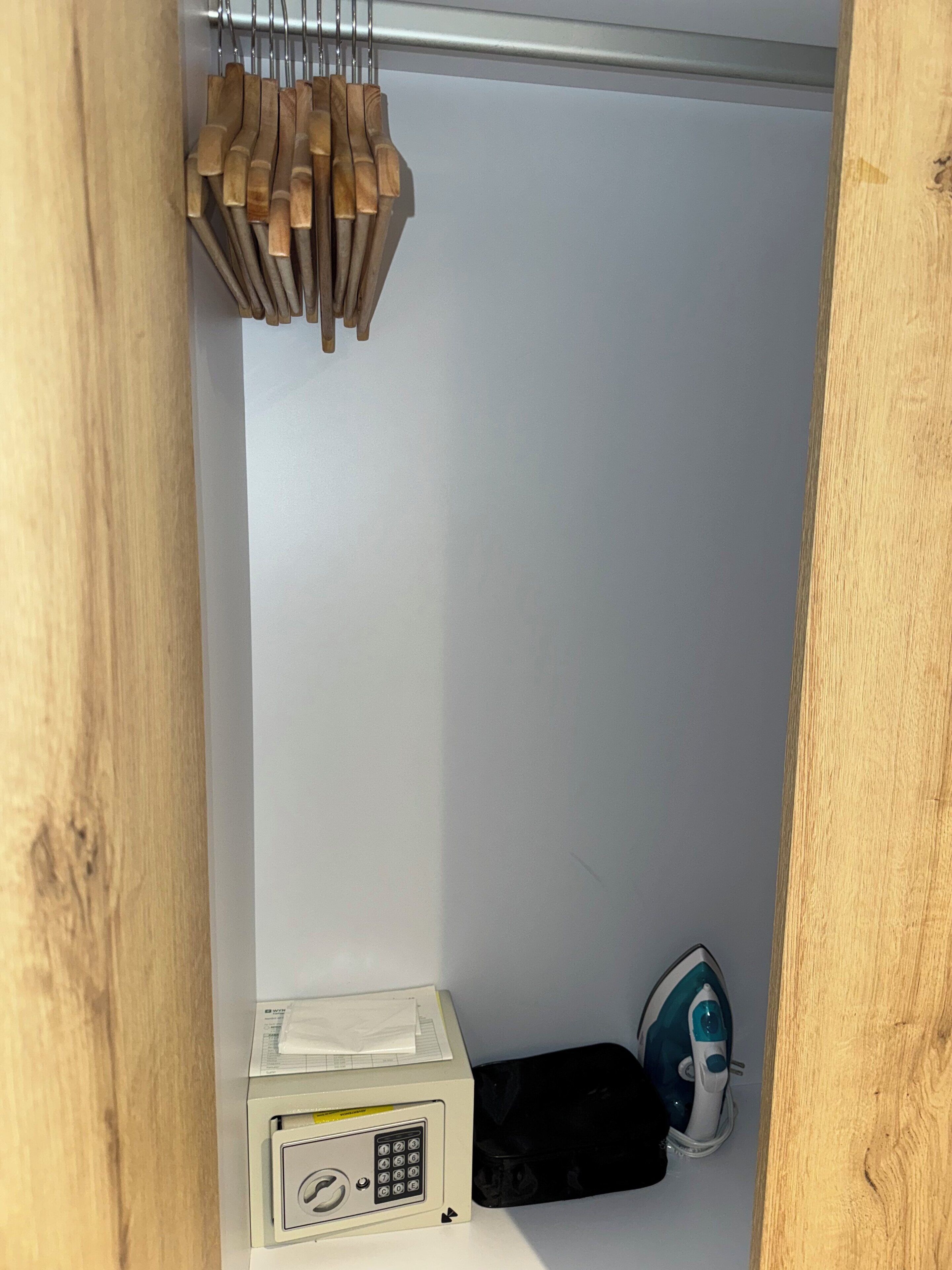 A small storage space with a microwave, an iron, and wooden-handled tools hanging on a rack.