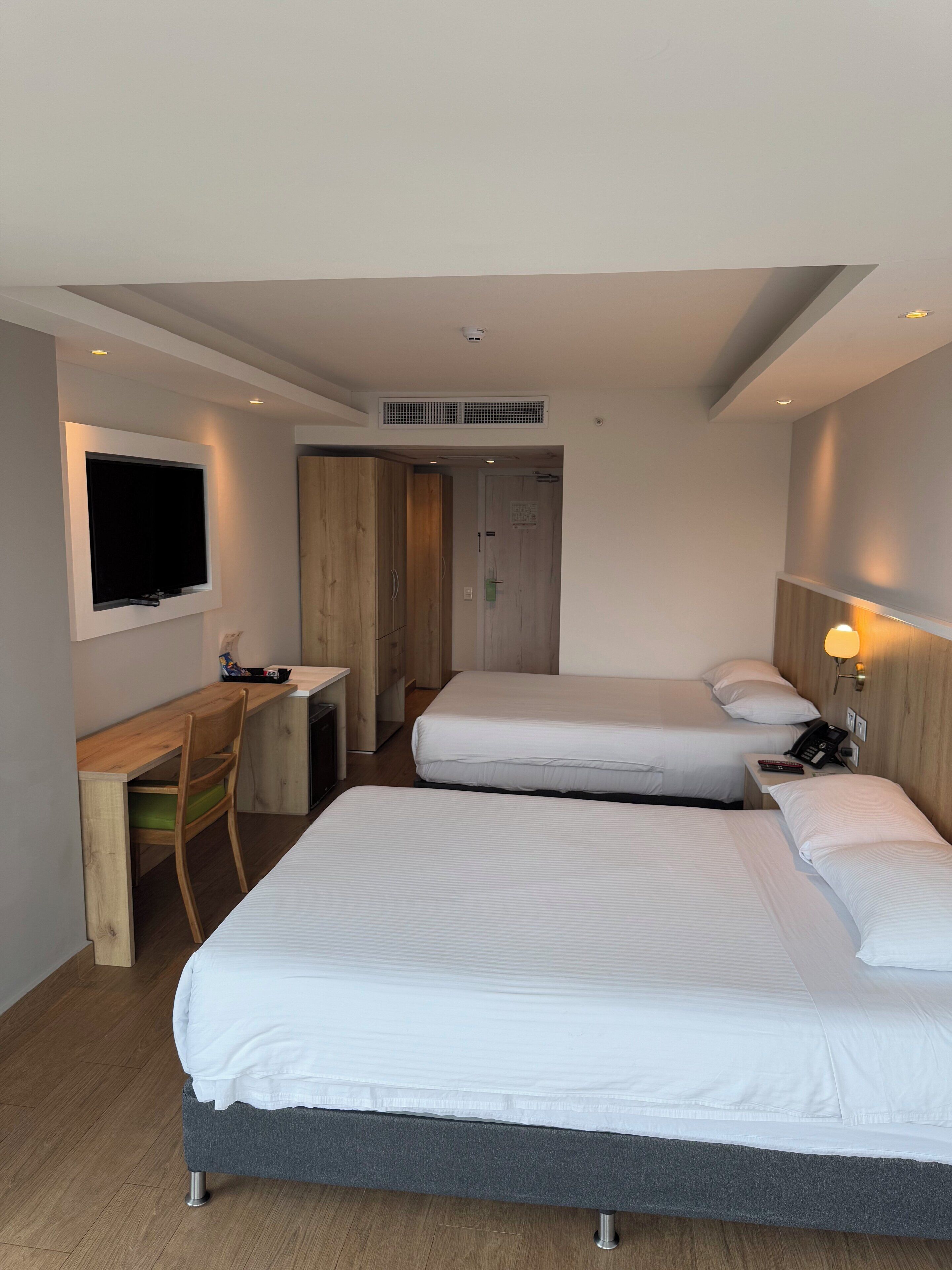 Une chambre d’hôtel avec deux lits simples, un bureau avec une chaise, un téléviseur fixé au mur et un téléphone sur la table de chevet.