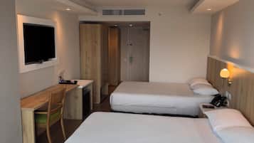 A hotel room with two single beds, a desk with a chair, a TV mounted on the wall, and a phone on the bedside table.