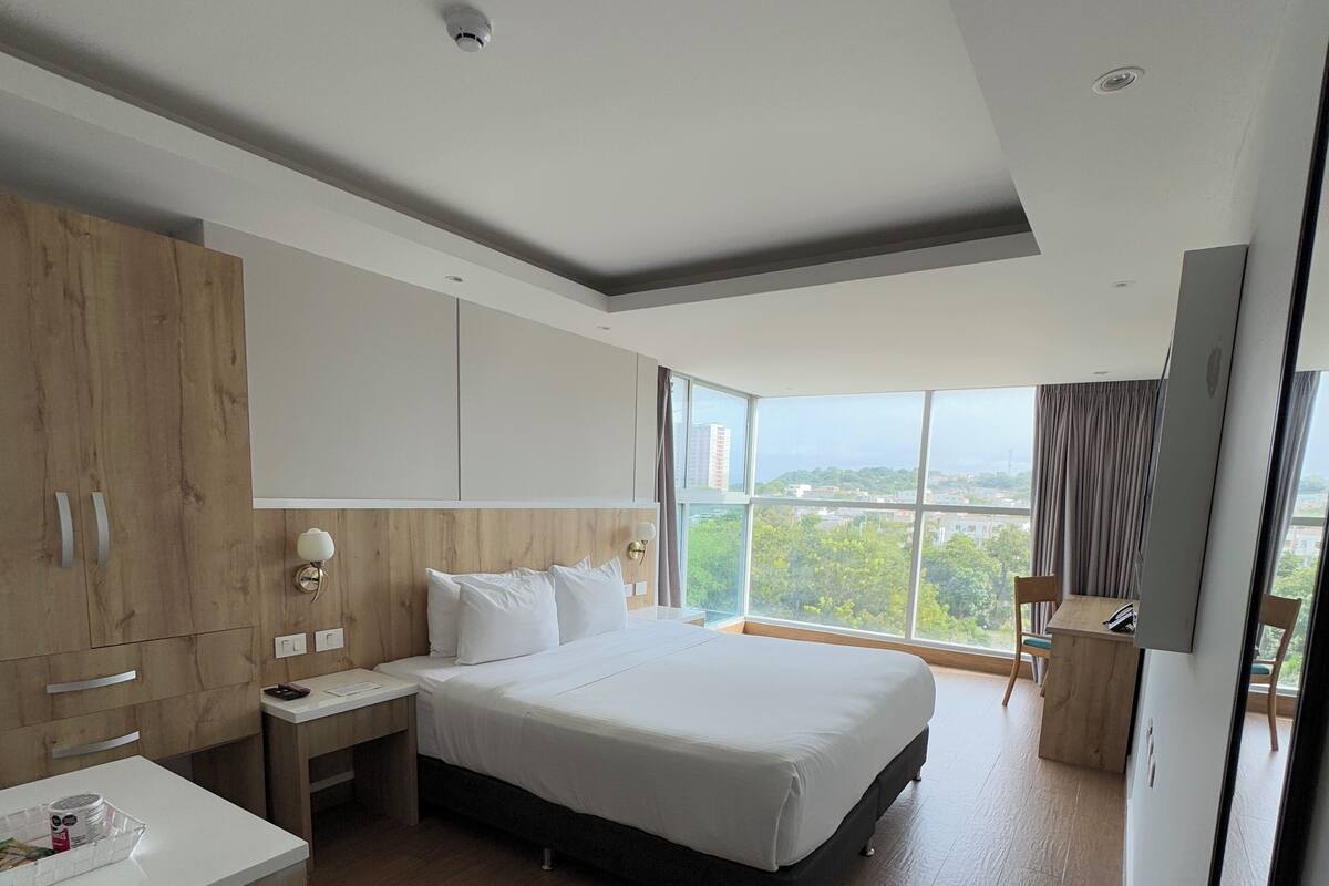 Een moderne hotelkamer met een groot bed, houten vloeren, een bureau en uitzicht op de stad.