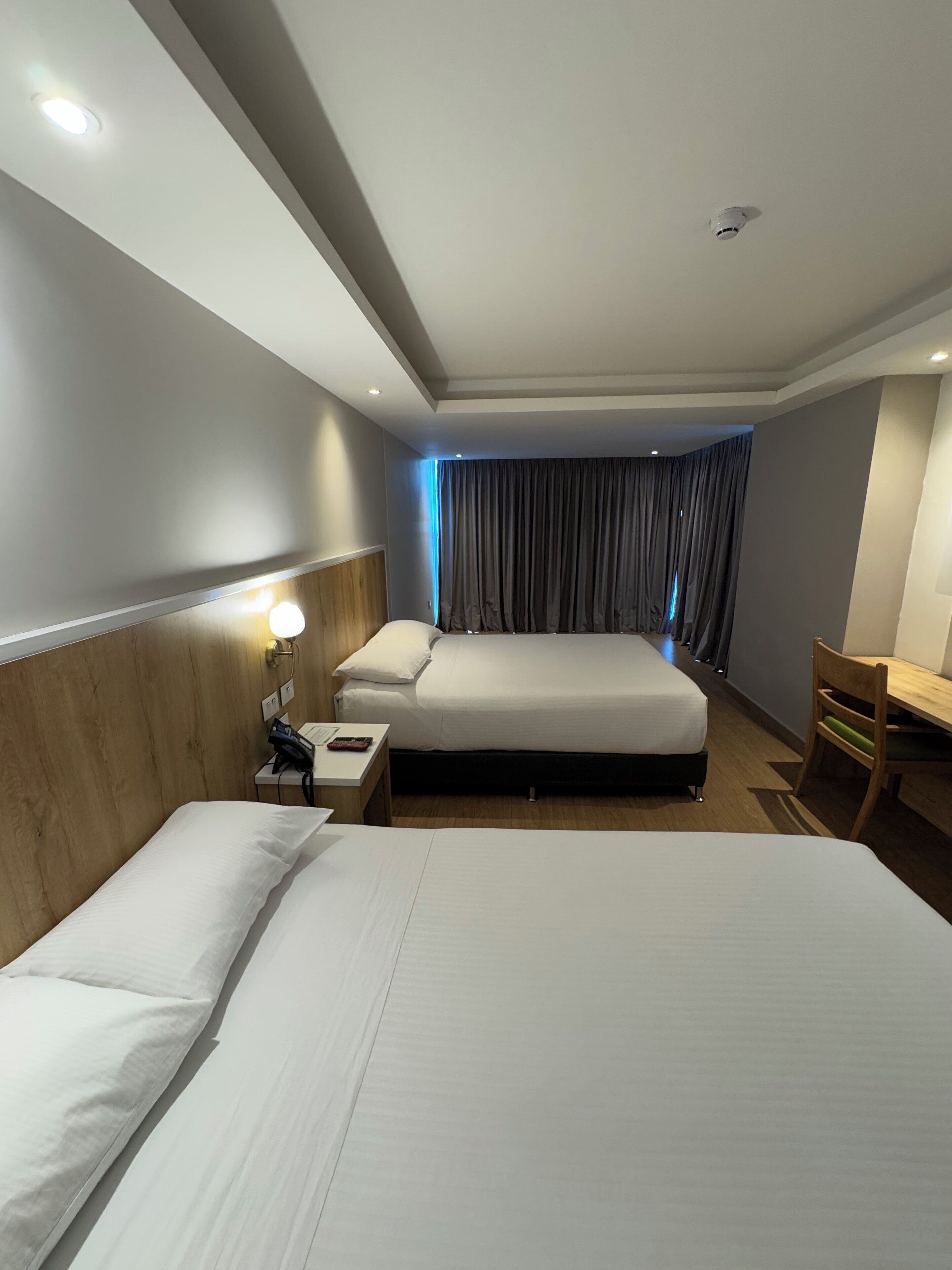 Habitación de hotel con dos camas, un escritorio, una silla, una mesita de noche con teléfono y una ventana con cortinas.