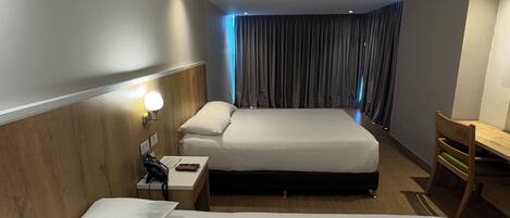 Habitación de hotel con dos camas, un escritorio, una silla, una mesita de noche con teléfono y una ventana con cortinas.