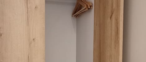 Un armario de madera con interior blanco, una barra para colgar ropa y un pequeño electrodoméstico blanco en la repisa inferior.