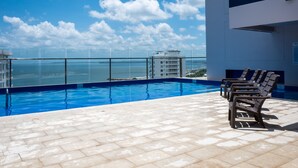 A rooftop pool with clear blue water, a glass barrier, and lounge chairs.