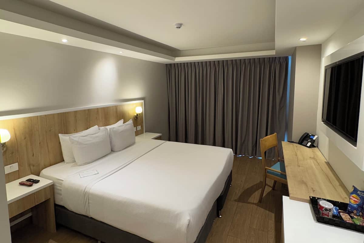 Een moderne hotelkamer met een groot bed, nachtkastje, lamp en een bureau met stoel.
