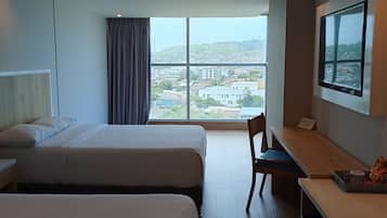 A hotel room with two beds, a desk, a chair, a TV, and a large window offering a city view.
