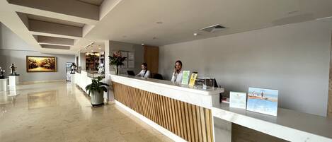 A modern reception area with a marble floor, a wooden reception desk, and a large painting on the wall.
