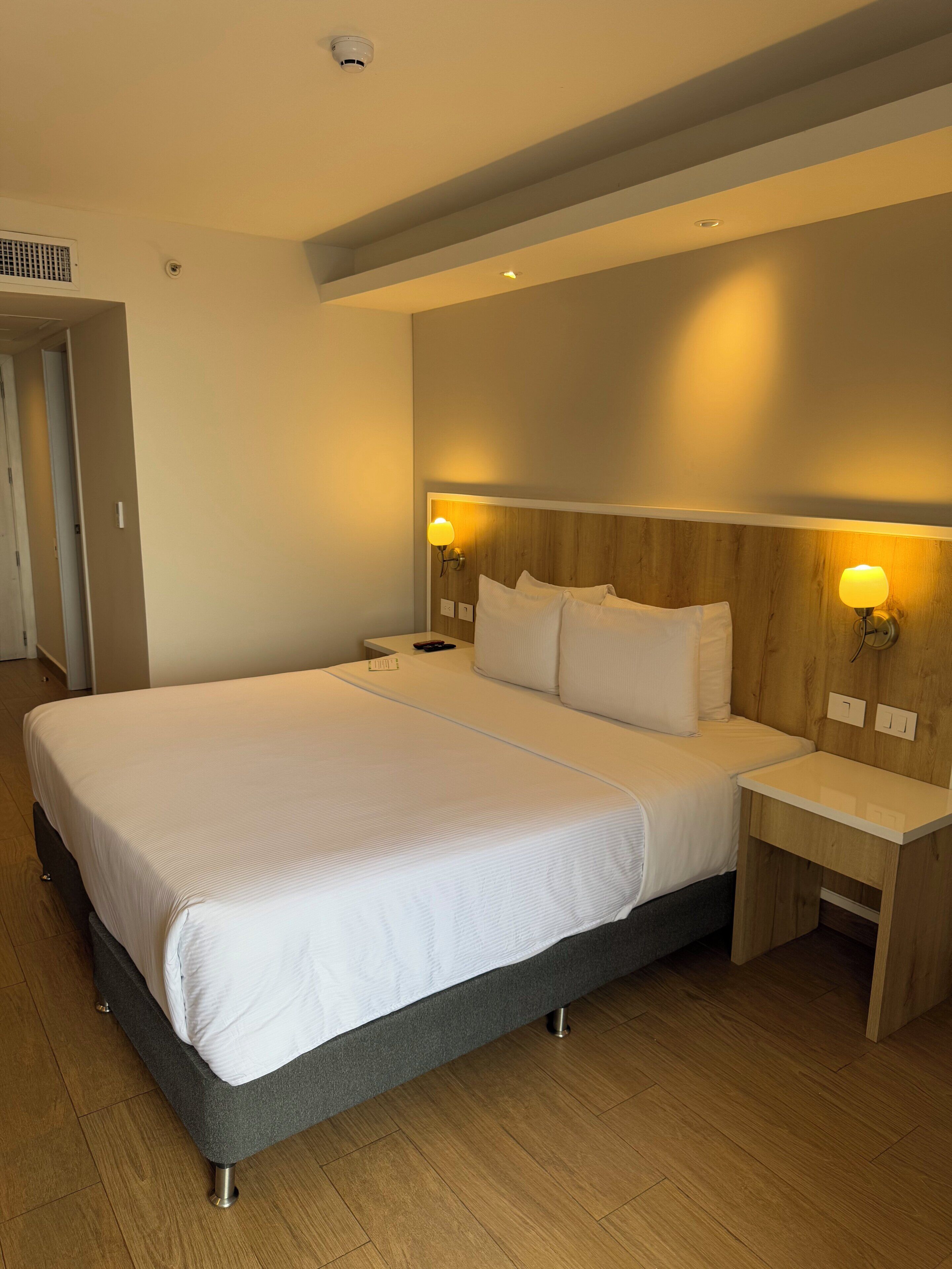 Ein modernes Hotelzimmer mit einem großen Bett, einem Holzkopfende, Nachttischlampen und Holzboden.