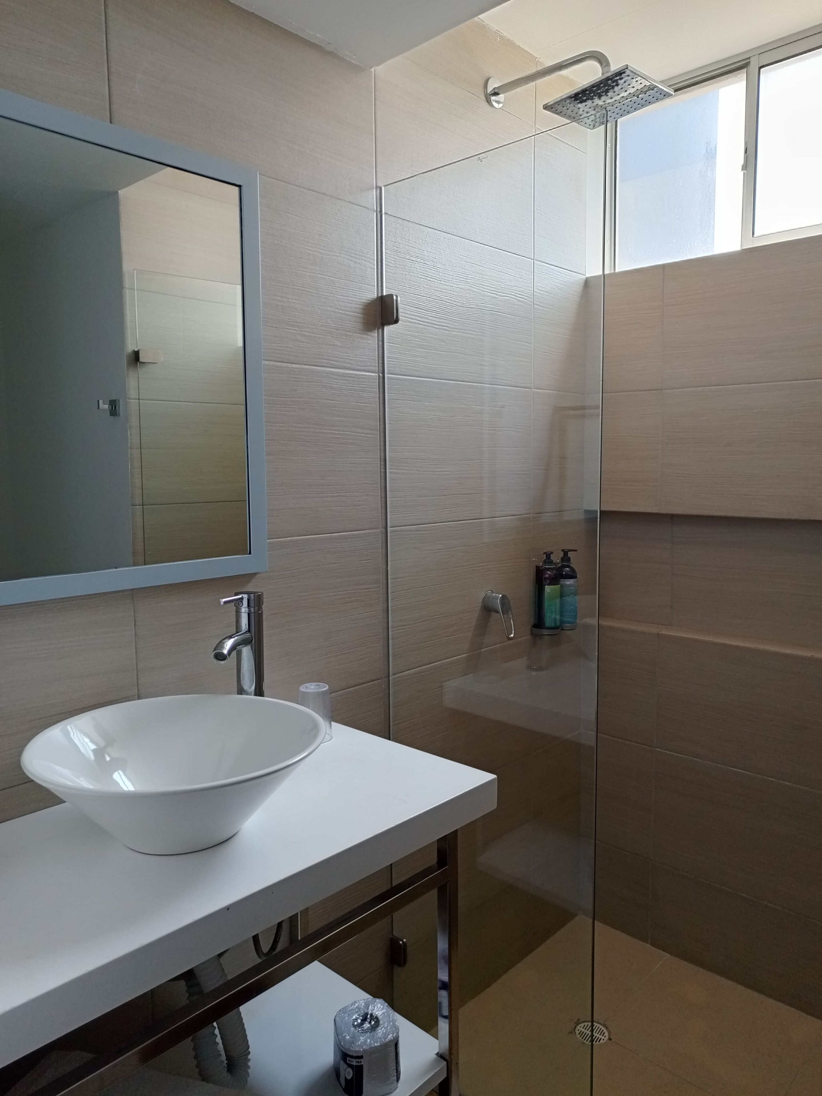 A modern bathroom with a white sink, a mirror, and a glass shower enclosure.