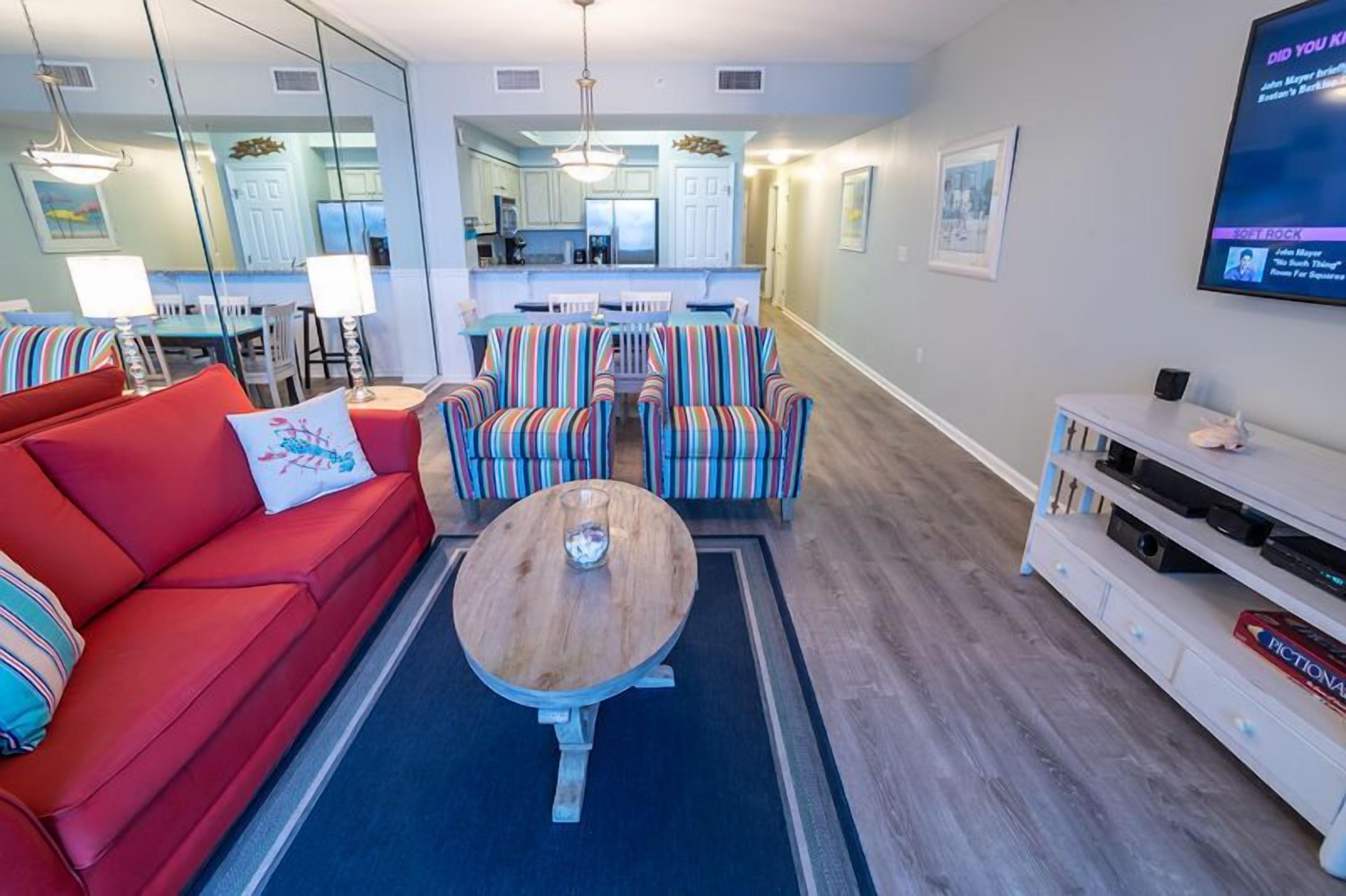 A modern living room with a red sofa, striped armchairs, a wooden coffee table, and a TV on a white stand.