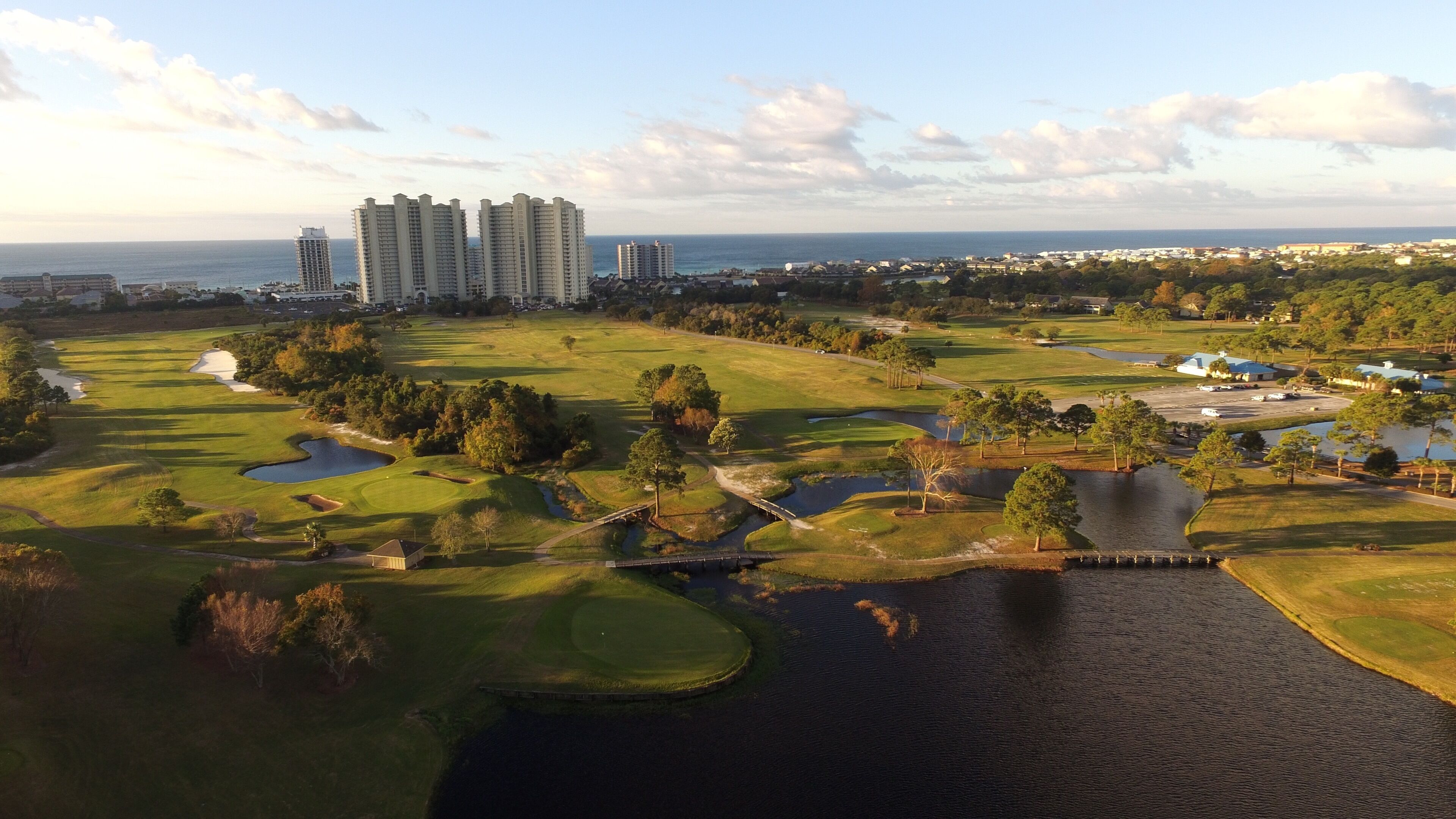 Golfkenttä, jossa on hiekkabunkkereita, vesiesteitä ja silta, joka ylittää lammen.