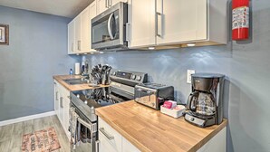 Eine kompakte Küche mit weißen Schränken, einer Edelstahl-Mikrowelle, einem Gasherd, einem Toaster und einer Kaffeemaschine.
