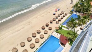 A beach resort with a swimming pool, beach umbrellas, and palm trees. - BEACHFRONT PENTHOUSE with PRIVATE POOL (Nuevo Vallarta)