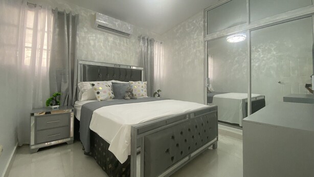 Un dormitorio moderno con cama, mesitas de noche, cómoda y un espejo grande.
