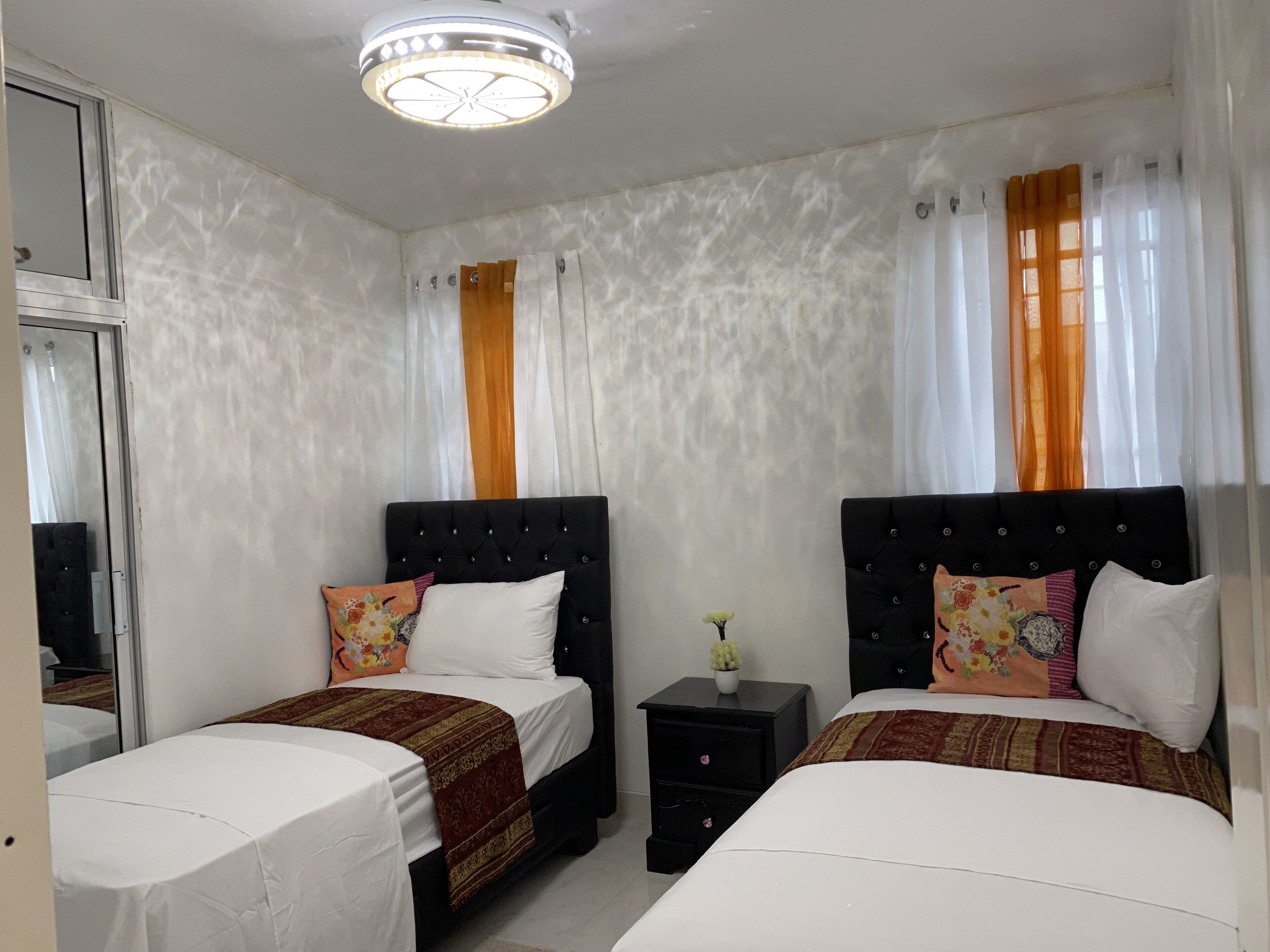 Habitación de hotel con dos camas, una mesita de noche pequeña, un espejo y una lámpara en el techo.