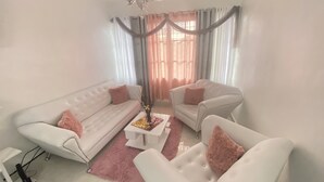 Un salón con un sofá blanco, un sillón blanco, una mesa de centro y una araña.