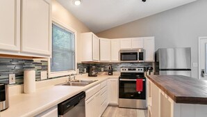 Una cocina moderna con armarios blancos, electrodomésticos de acero inoxidable, lavavajillas y encimera de madera.