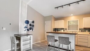 Una cocina moderna con una isla central, dos taburetes de bar y una mesa de comedor con sillas.