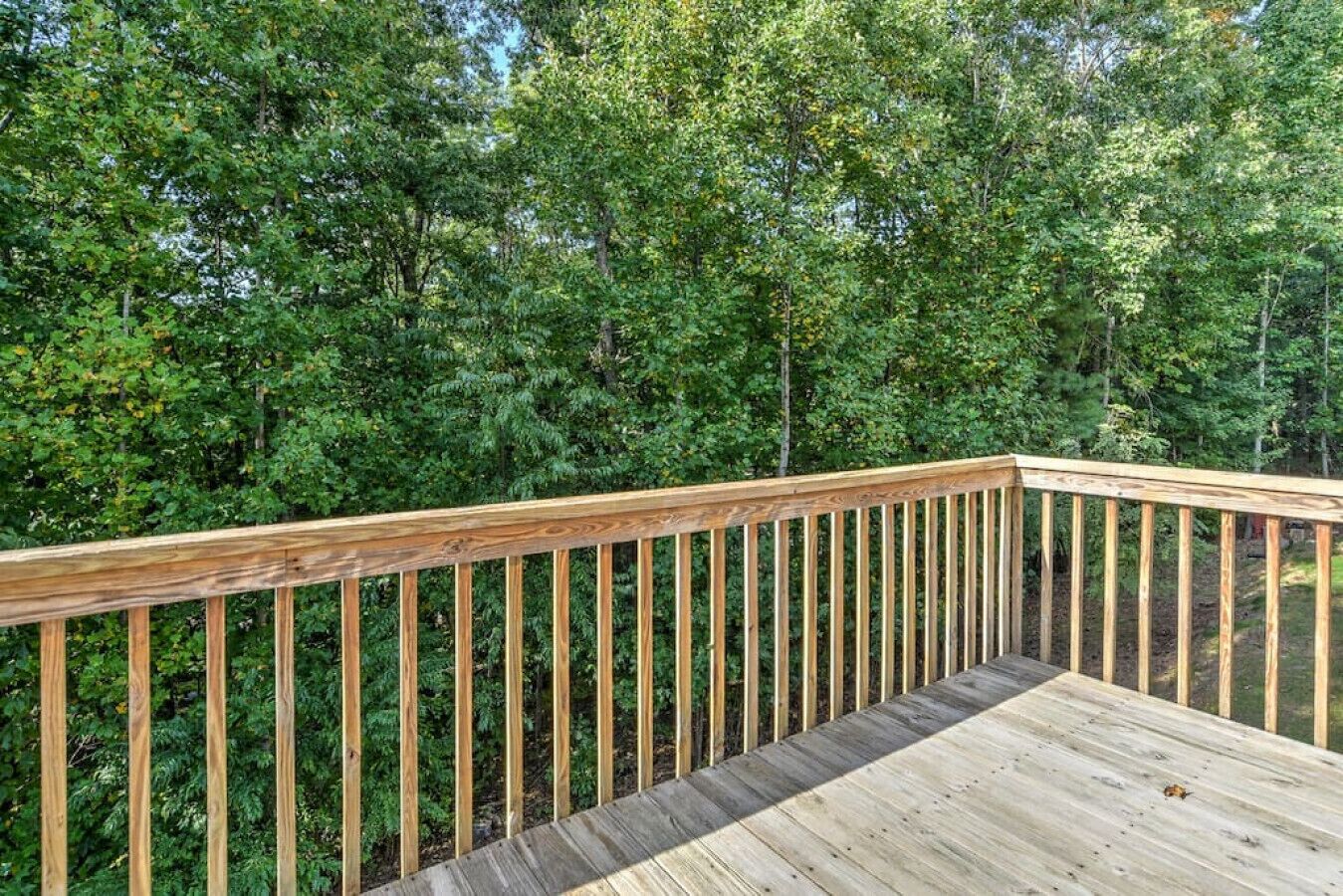 A wooden deck with a railing overlooking a dense forest.