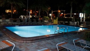 Ein Schwimmbad mit Liegestühlen und Palmen bei Nacht.