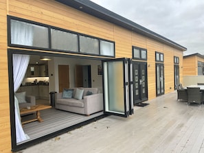 A modern wooden building with a sliding glass door leading to a living area with a sofa and a dining table.