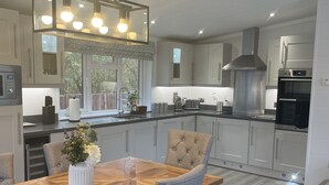A modern kitchen with a central island, stainless steel appliances, and a dining area with a wooden table and grey upholstered chairs.