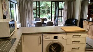 A compact kitchen with a Bosch washing machine, a microwave, and a wooden cutting board on the countertop. - Queen Charlotte Secret Oasis, Marlborough Sounds. (Linkwater)