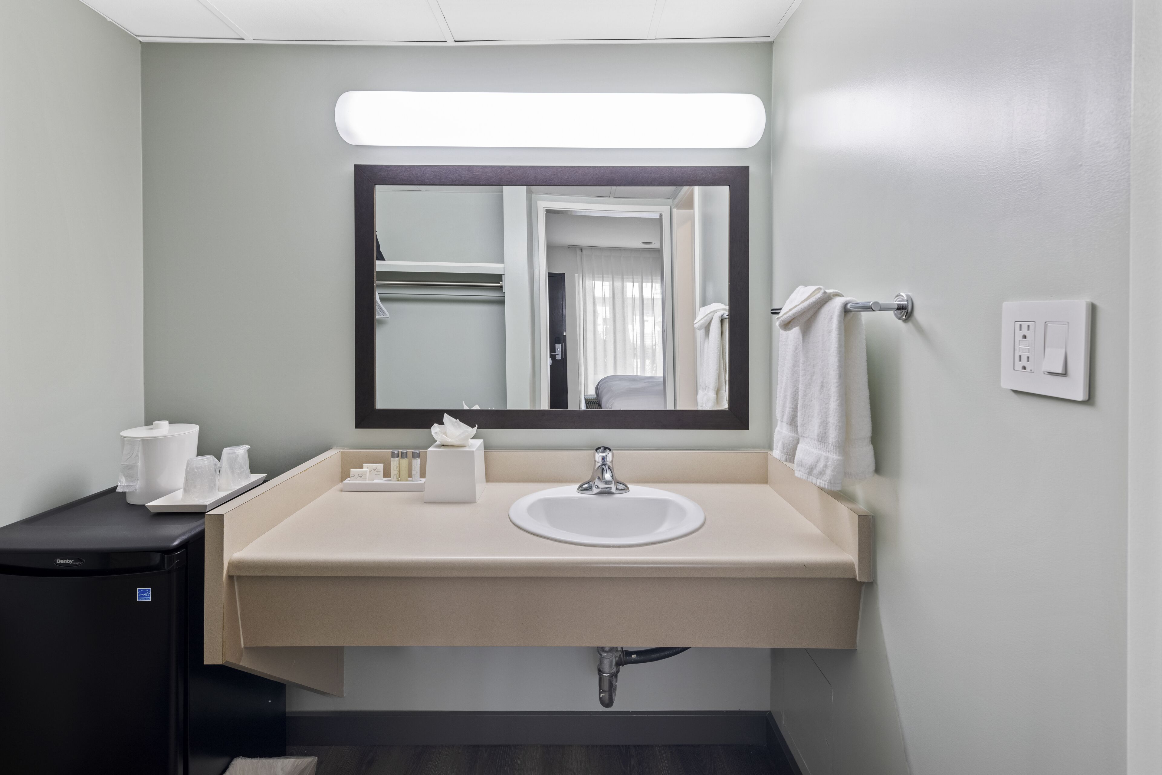 Een badkamer met een wastafel, spiegel, handdoekrek en een klein kastje met toiletartikelen.