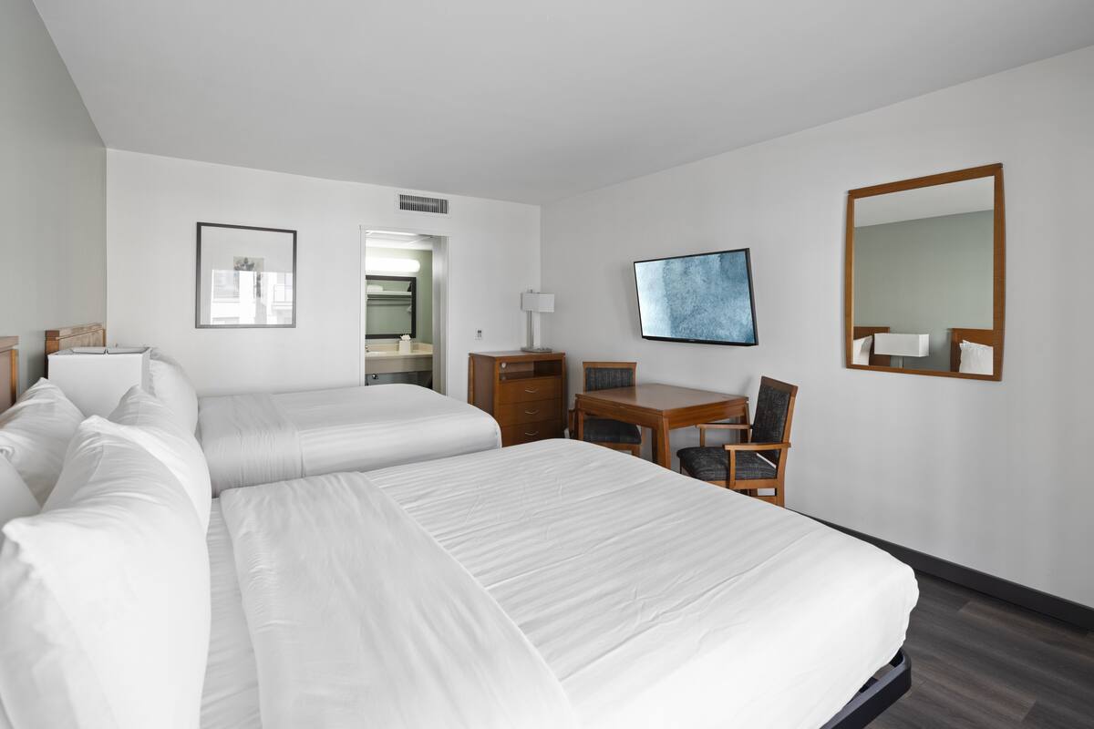 A hotel room with two beds, a desk, a chair, a TV, and a mirror.