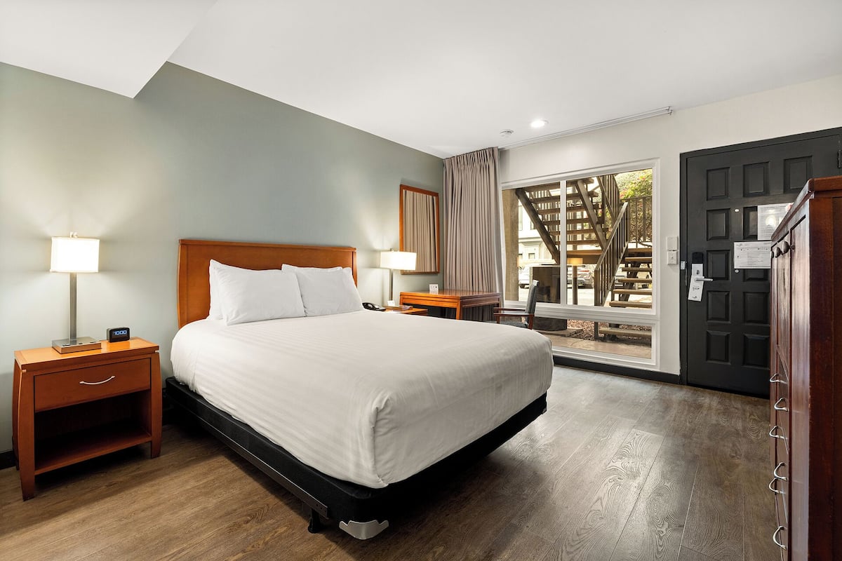 A hotel room with a large bed, wooden nightstands, a desk, and a view of the outside through a glass door.