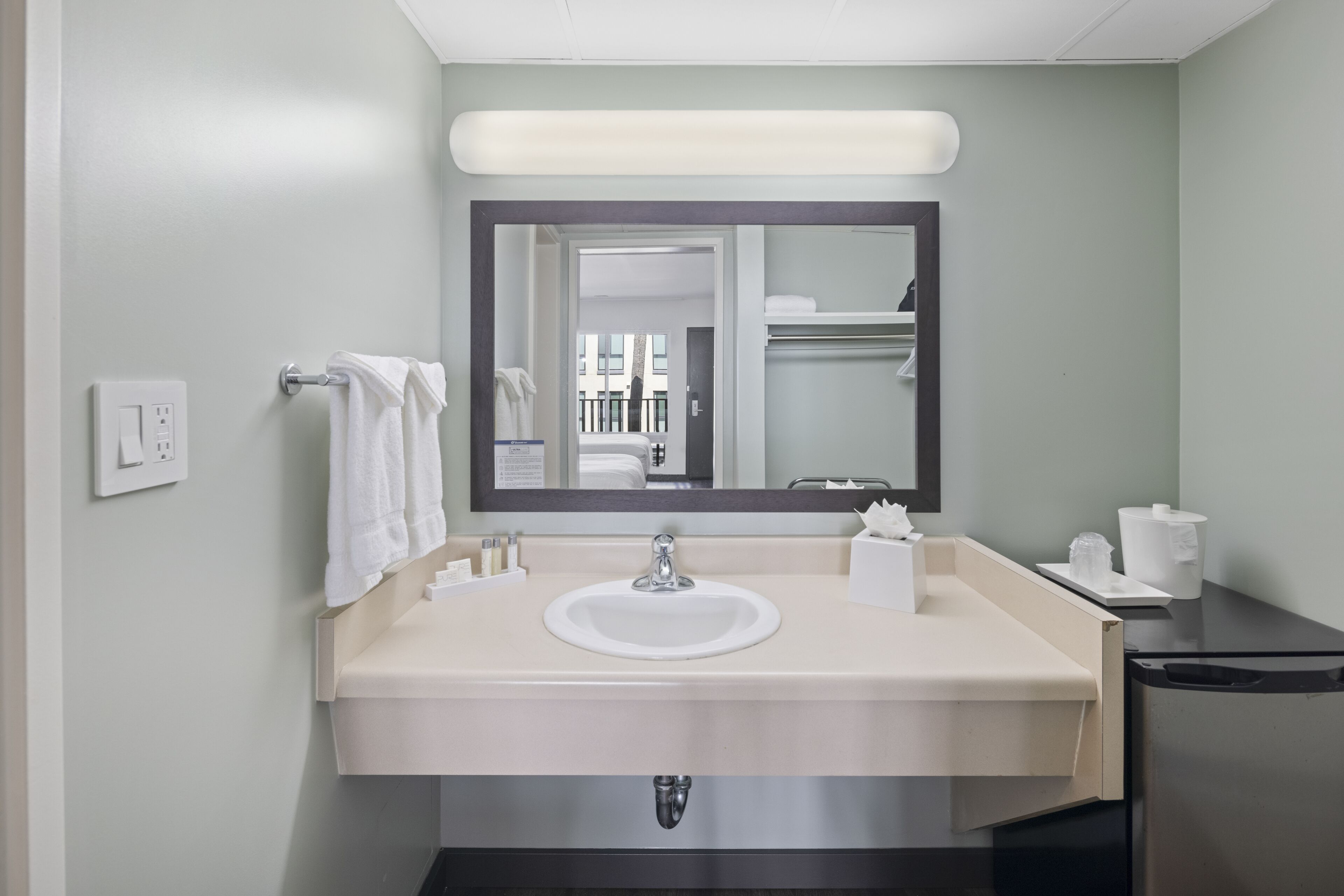 Une salle de bain équipée d’un lavabo, d’un miroir, d’un porte-serviettes et d’articles de toilette.