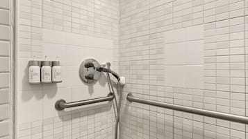 A shower area with white tiled walls, a handheld showerhead, a handheld shower attachment, and a bench.