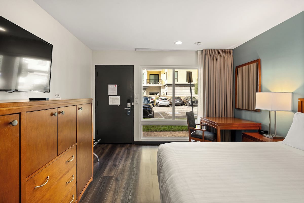 A hotel room with a bed, a desk, a TV, and a view of the street outside.