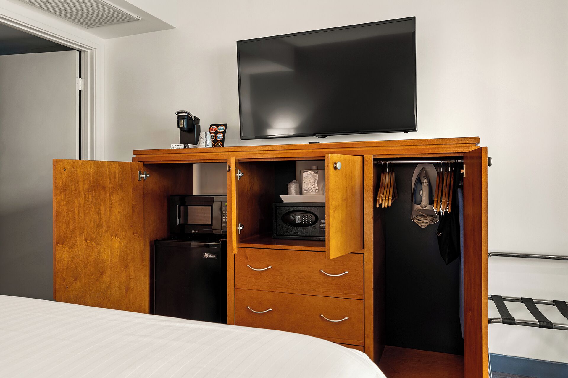 Een slaapkamer met een bed, een kledingkast met een televisie erboven en een magnetron in de kast.