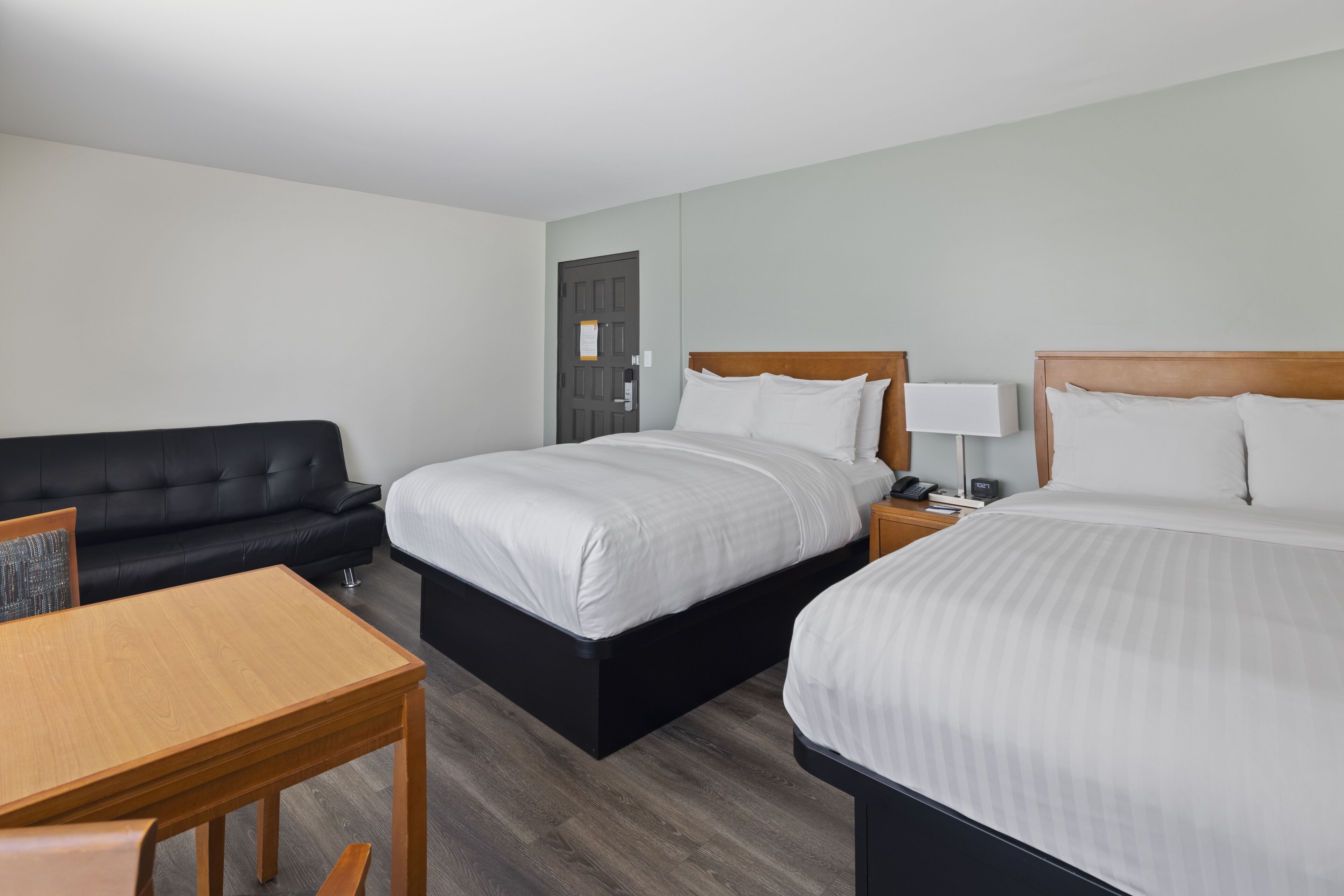 A hotel room with two beds, a sofa, a wooden table, and a nightstand with a lamp.