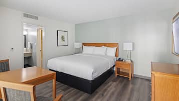 A hotel room with a large bed, a bedside table with a lamp, a wooden desk, and a chair.