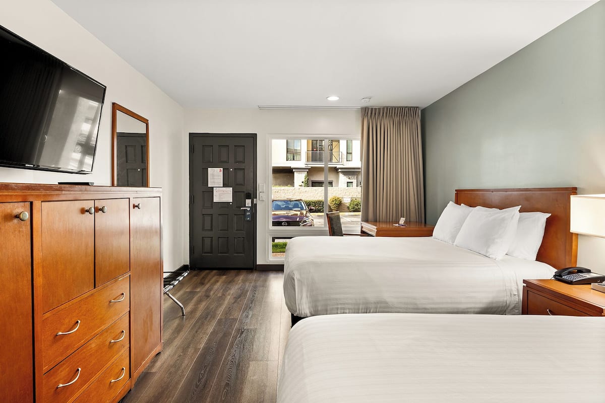 A hotel room with two beds, a TV, a wooden dresser, and a view of the street.