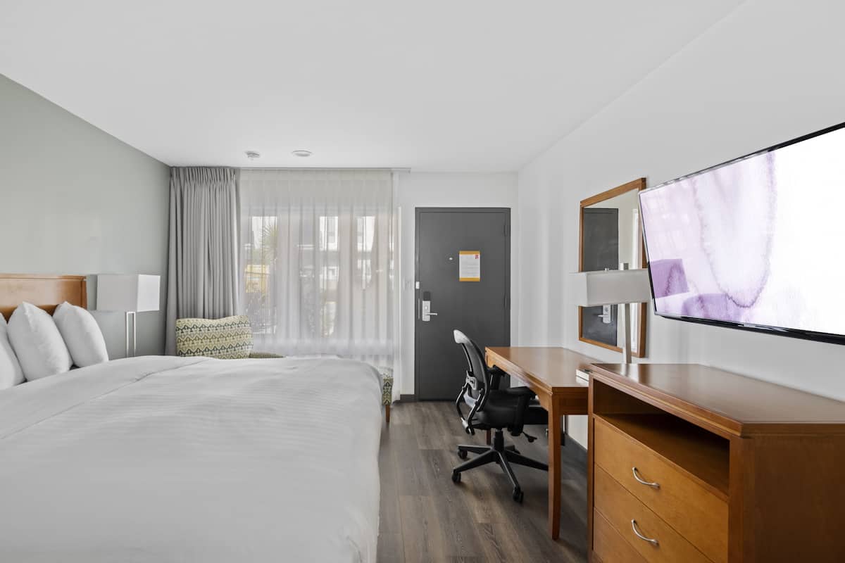 A hotel room with a bed, a desk, a chair, a TV, and a door with a mirror.