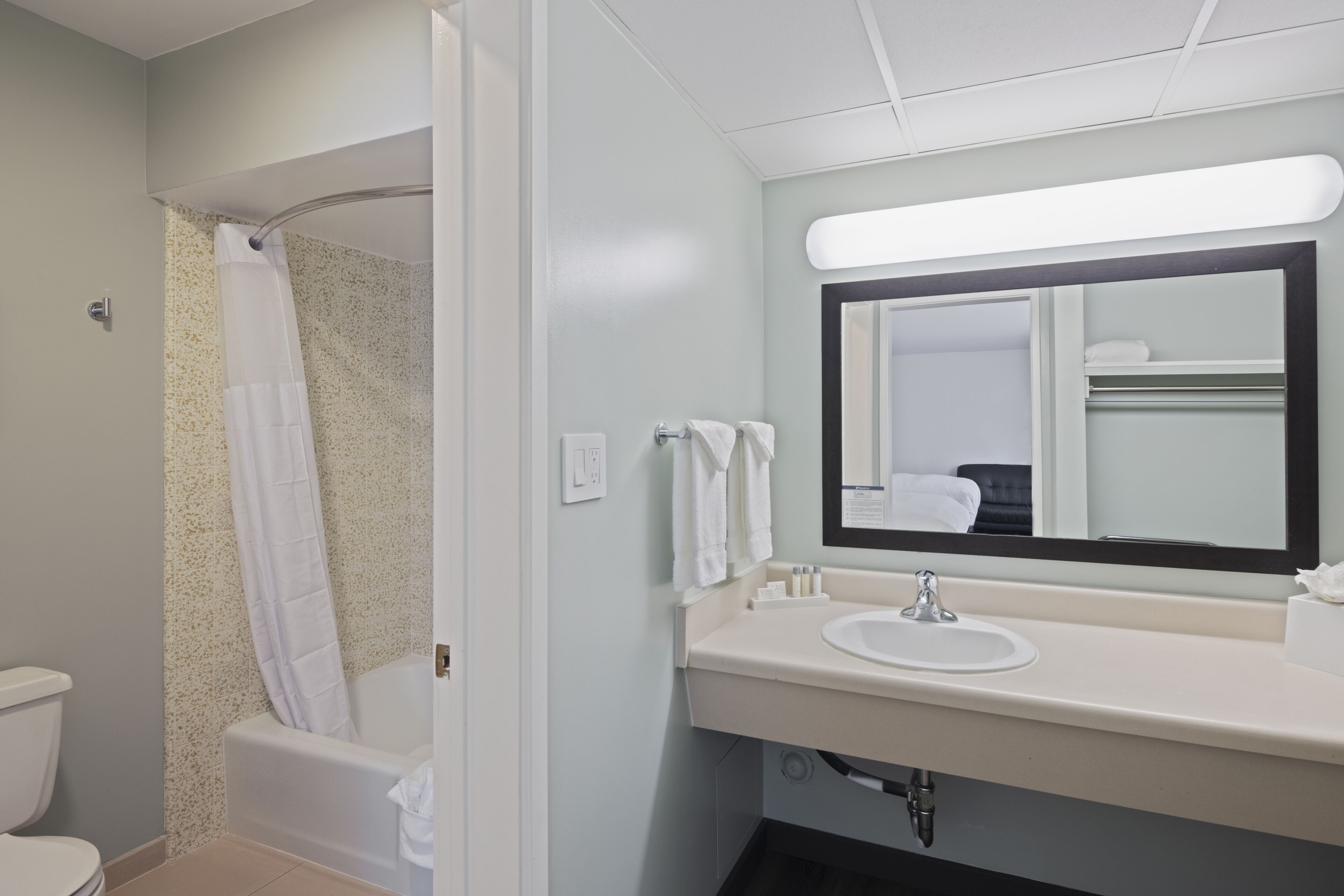 A bathroom with a shower, toilet, sink, and mirror.