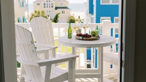 Un balcon avec des chaises blanches et une table où sont disposées des bouteilles et des grappes de raisin.