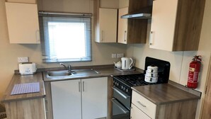 Een kleine keuken met een gasfornuis, een spoelbak en een raam met jaloezieën.