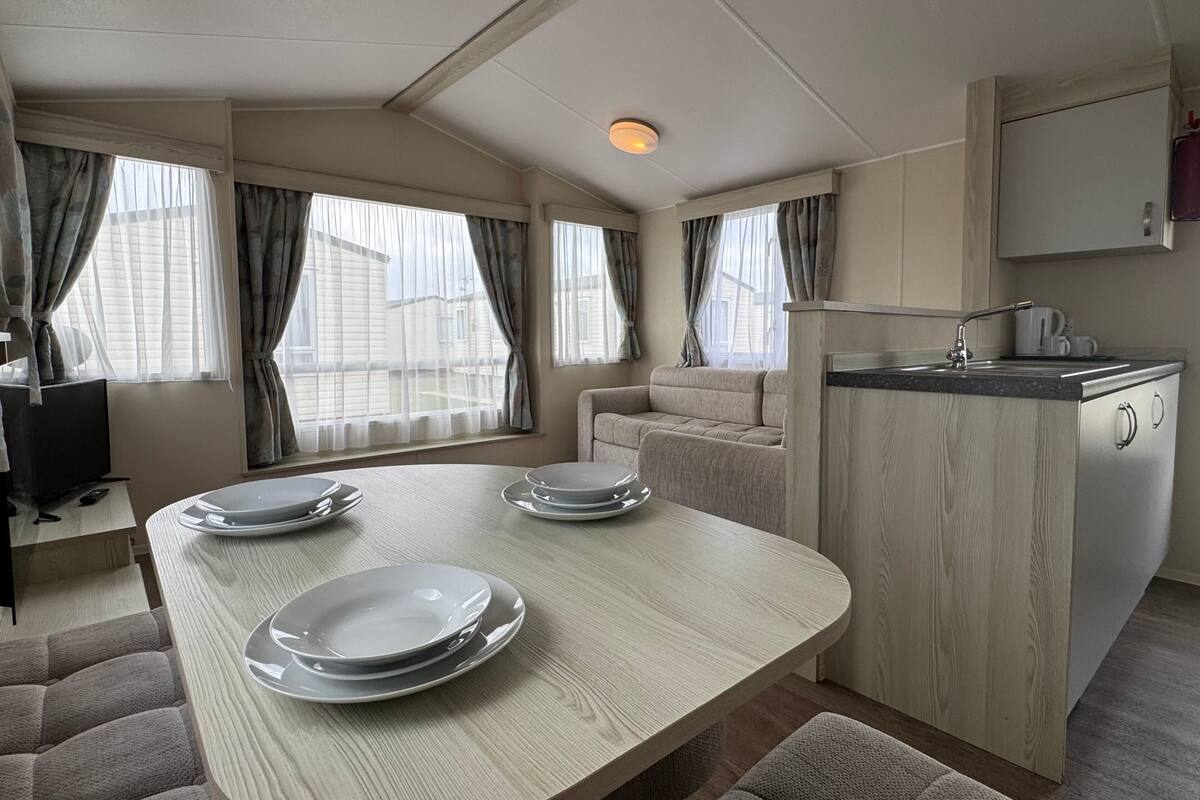 A compact kitchen with a dining area, featuring a wooden table, a built-in sink, and a sofa.