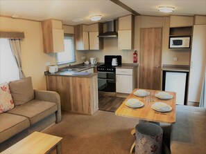 A compact kitchenette with a stove, microwave, and sink. There is a dining area with a table set for four. - Towervans Holiday Park (Mablethorpe)