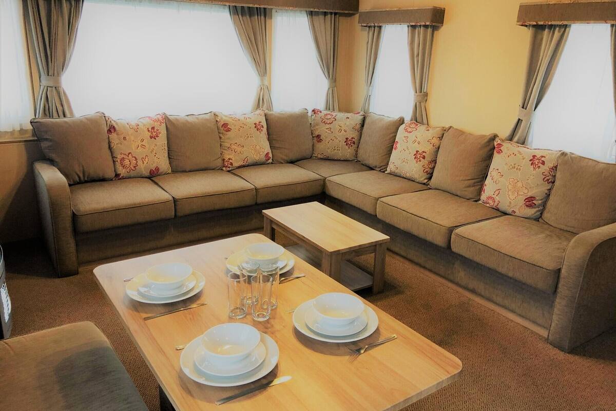 A cozy living room with a sectional sofa, a wooden coffee table, and a dining table set with plates and glasses.