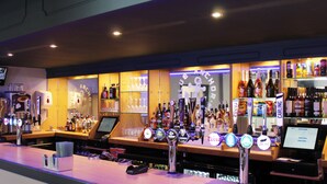 Een bar met meerdere biertaps, een scherm en planken vol verschillende flessen.