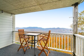 Un balcon avec deux chaises en bois et une table, donnant sur un paysage montagneux.