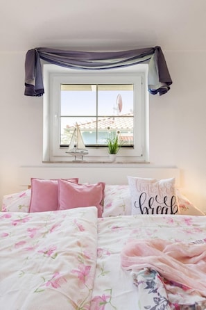 A bedroom with two beds, a window with a view of the sea, a small sailboat model, and a potted plant. - Am Bahndamm 73 "Haus Meerblick" - bright and friendly vacation home in (Zingst)